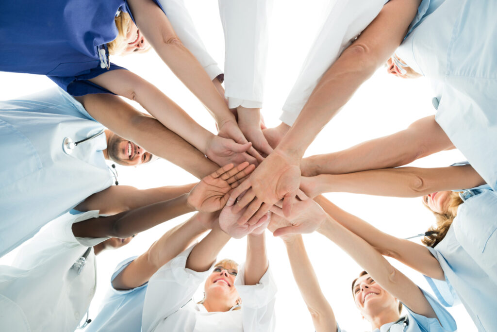 Hände von Pflegekräften aus verschiedenen Ländern übereinander als Zeichen für Teamarbeit